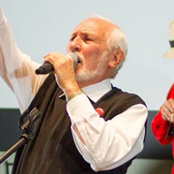 Photo of Bill Exley holding microphone with arm in the air