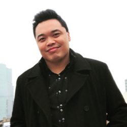 Photo of Chris Dela Torre outdoors wearing black jacket and smiling