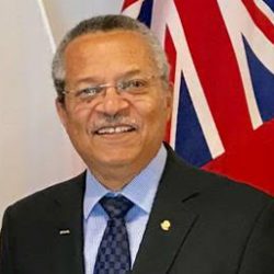 Photo of Harold Usher in suit and tie smiling infront of Ontario flag