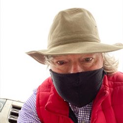 Photo of James Reaney in brimmed hat, bright red vest and medical mask