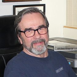 Photo of Roland Schubert sitting at desk in blue t-shirt